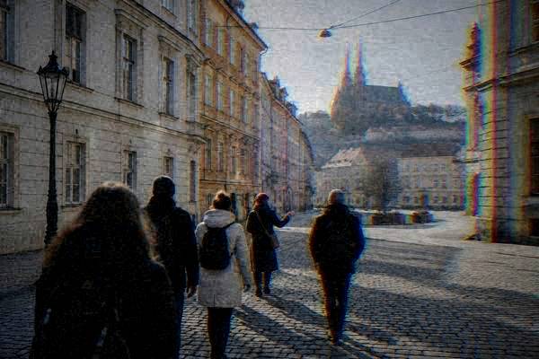 A small walking group crossing a small cobbled square behind a guide, tall cream and ochre townhouses and tram wires overhead, Brno old town
