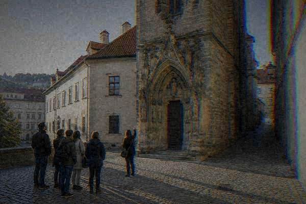 A guide gesturing up at a carved stone portal at the foot of a Gothic tower while a small group stands back on the cobbles, Old Town Hall