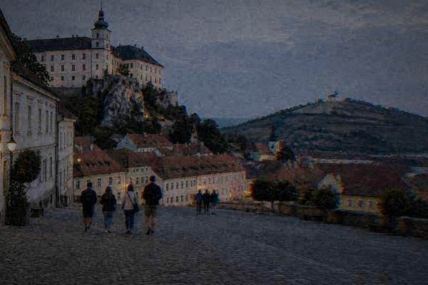 A small group of day visitors walking a broad sloping square under a white chateau on a rock, vineyards on the slopes beyond, Mikulov