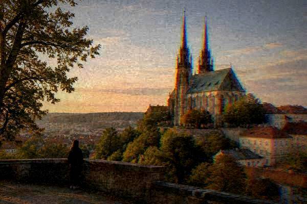 A visitor small in the frame on a stone terrace looking up at a Gothic cathedral with two tall slim spires on a wooded hill, Cathedral of Saints Peter and Paul