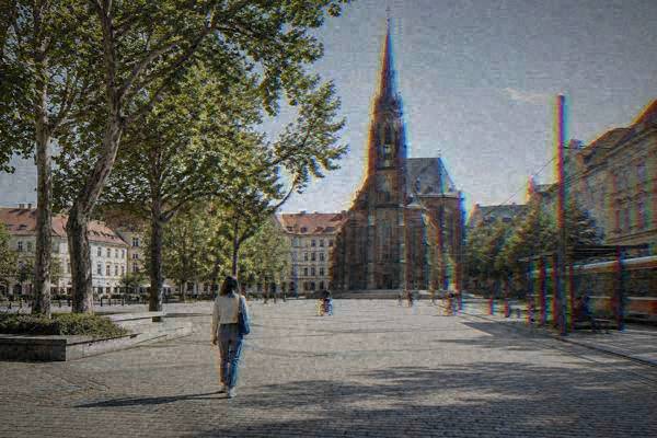 A lone visitor walking across a wide square toward a Gothic brick church with a slender spire, a tram stop and old plane trees, Old Brno