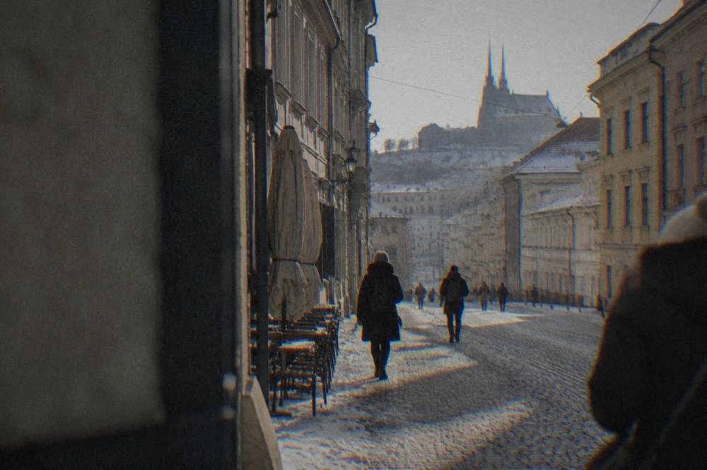 People walking along a snow-dusted street in central Brno past closed café fronts