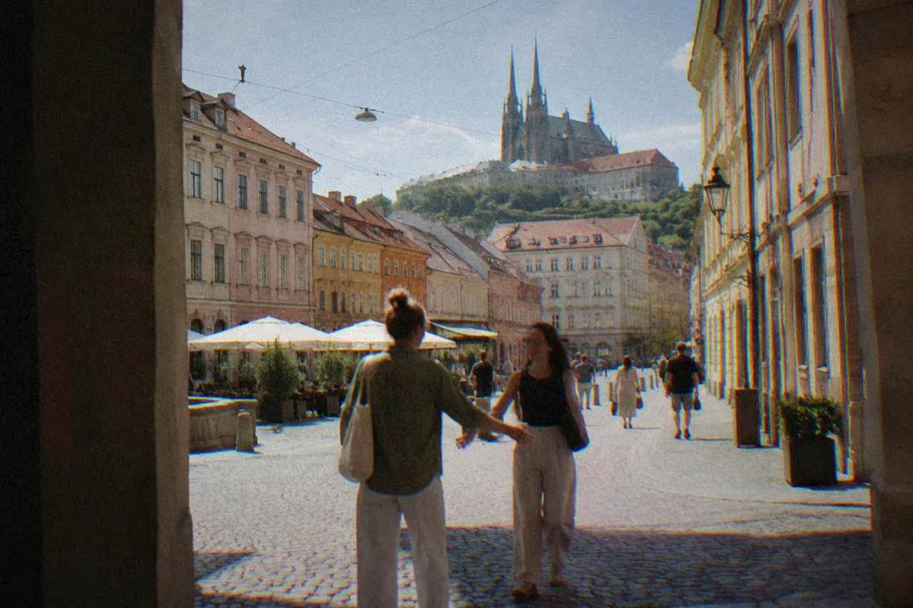 Two people greeting each other on a historic Brno square lined with colourful facades