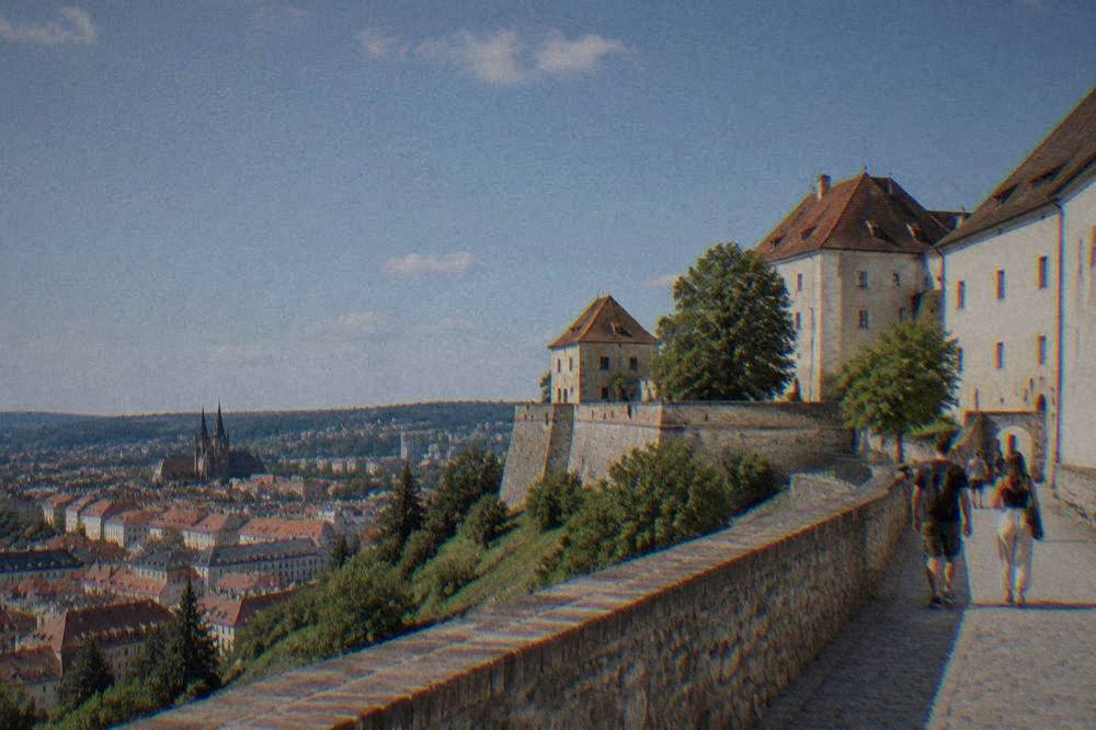 Visitors walking along the stone ramparts of a castle with views over red rooftops