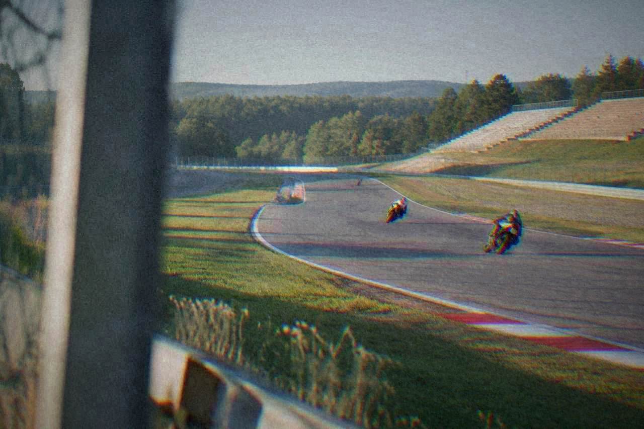 Grand Prix motorcycles at speed on a tree-lined circuit