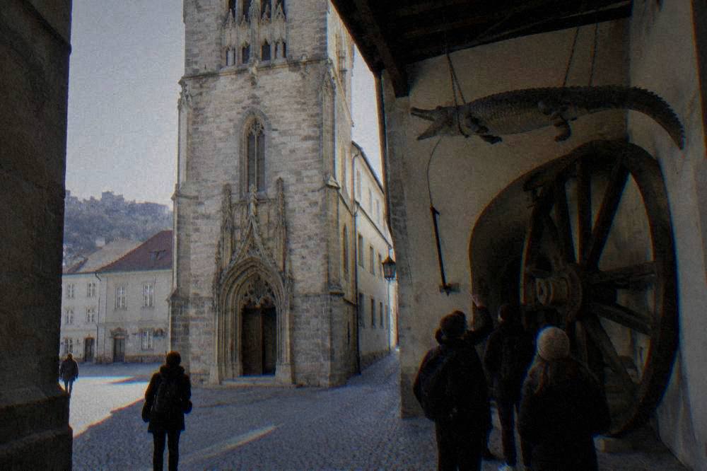 Visitors looking up at the hanging crocodile and the large wooden wheel in the Old Town Hall passage in Brno