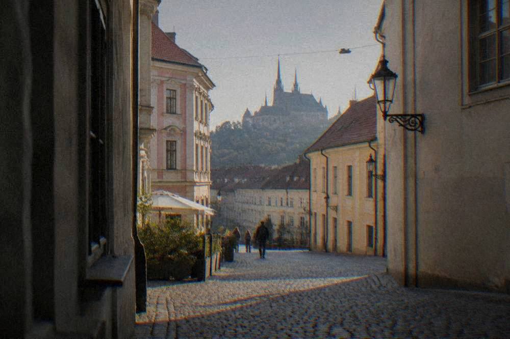 A cobbled lane in Brno old town with colourful baroque buildings and a church spire behind