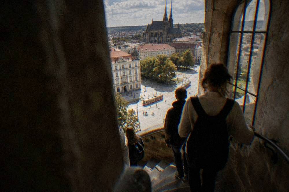 Visitors climbing a narrow stone spiral staircase inside an old Brno tower