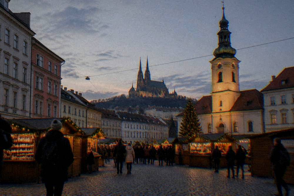 A Brno square at dusk with lit market stalls and a illuminated church tower