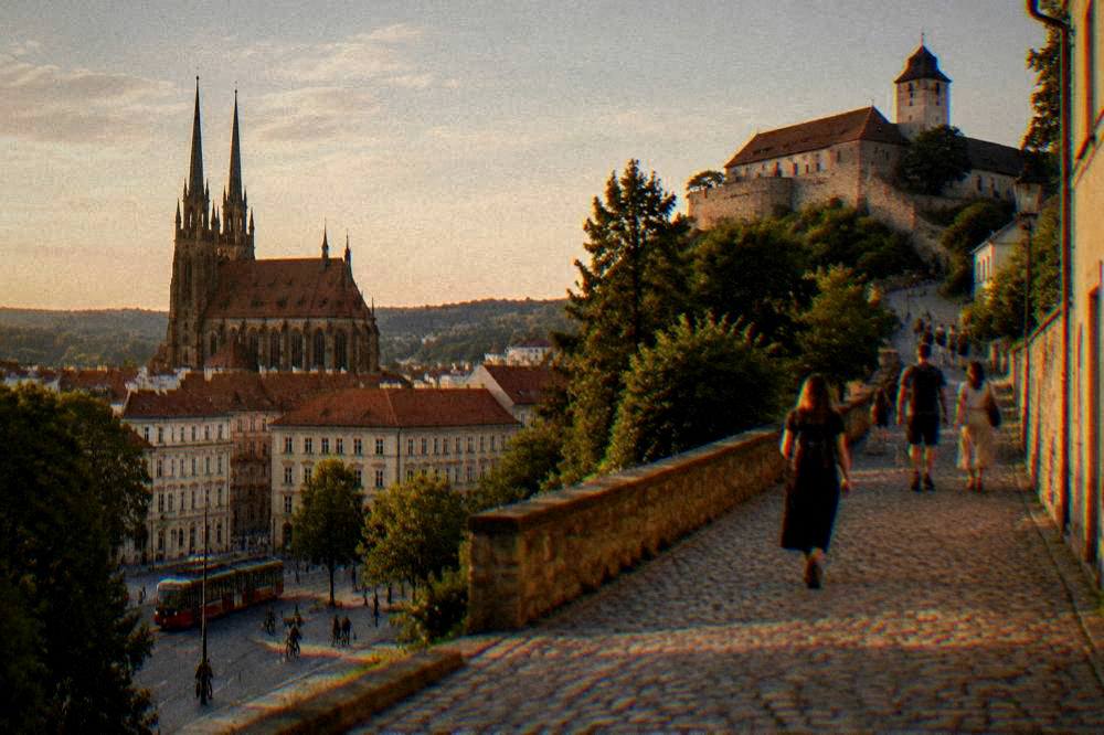 Visitors walking up a cobbled lane toward a fortress on a hill above a city