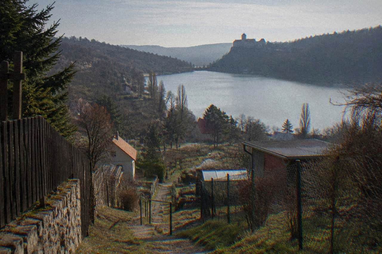 A wide lake surrounded by wooded hills, with a castle on a promontory in the distance