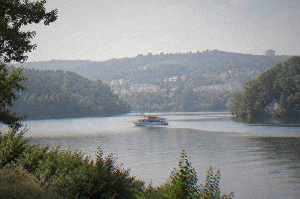 A passenger boat crossing a calm lake between forested banks