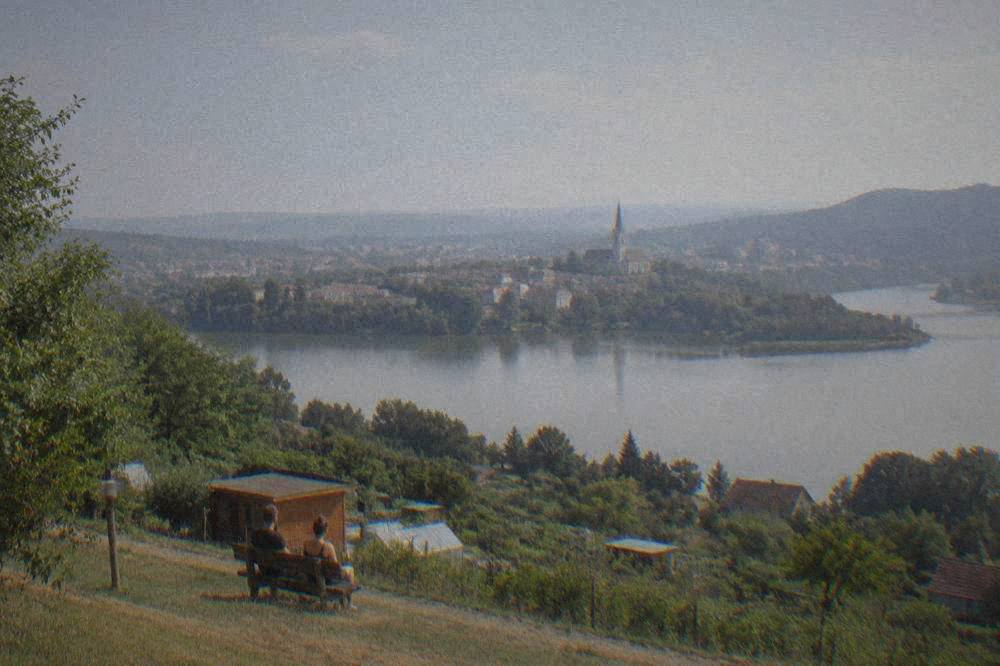 A hilltop view over a lake at midday, with a small town and church tower across the water