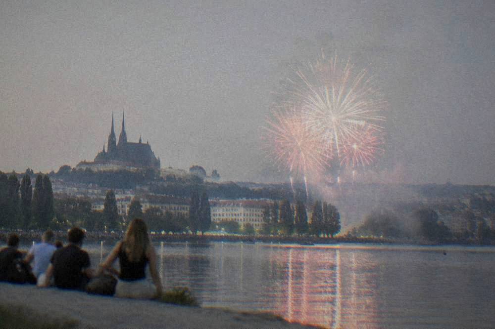 Evening fireworks over a lake with crowds on the shore