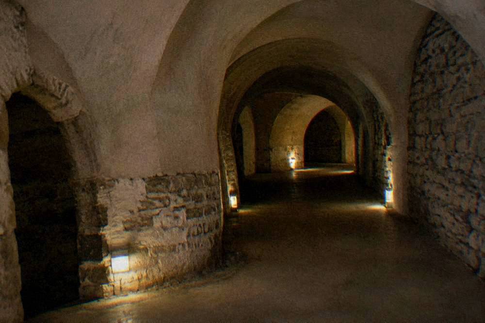 A narrow stone passageway underground lit by small lamps