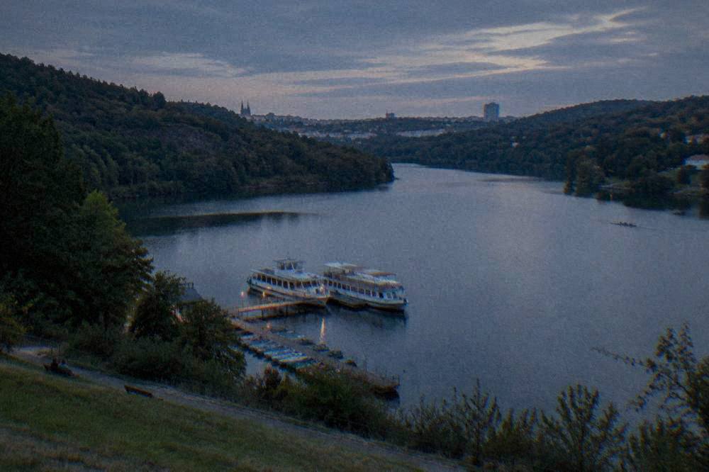 A forested valley with calm grey water winding between tree-covered slopes under a cloudy sky