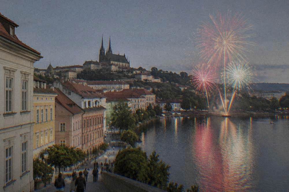Fireworks bursting in colours above a dark lake with a crowd watching from the far shore