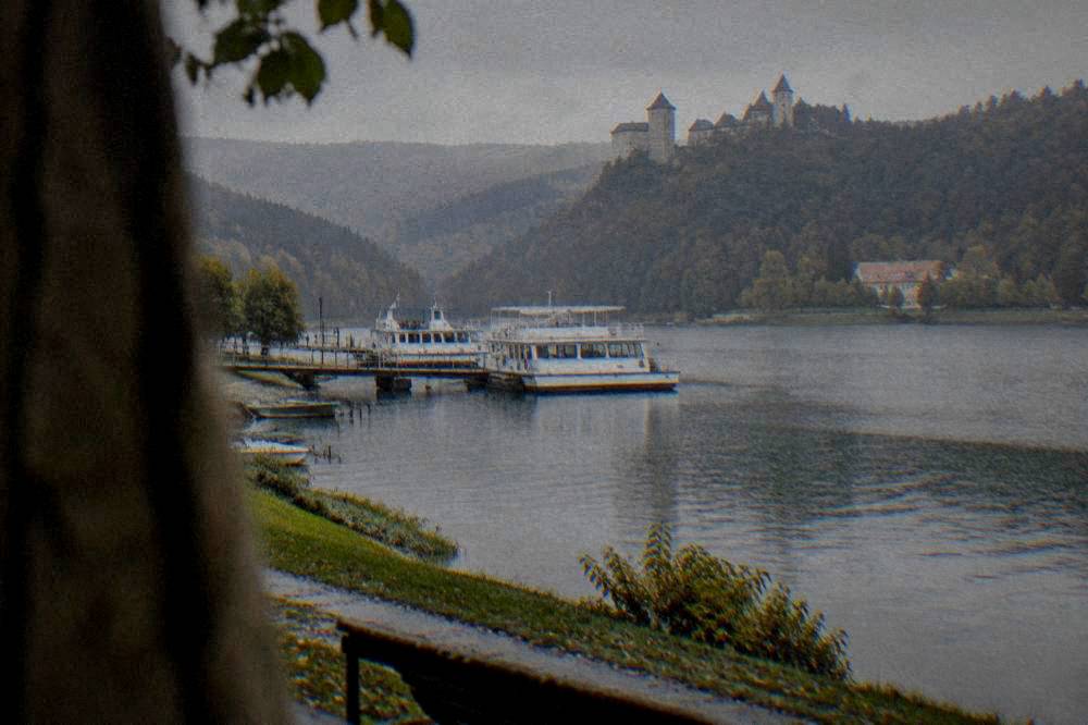 A stone castle with towers standing on a wooded ridge above a lake