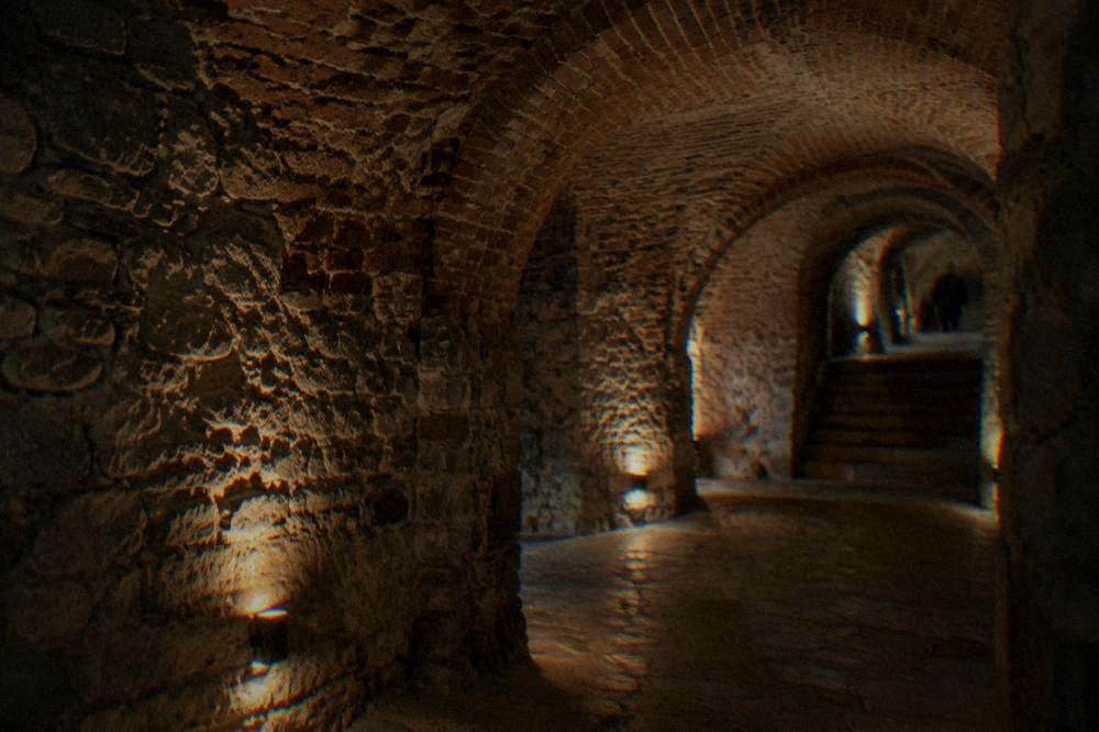 Dimly lit underground chamber with stacked stone and brick vaulting beneath a church