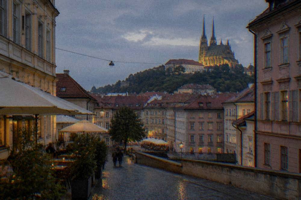 Evening view of a church spire illuminated above old town rooftops with cafés below