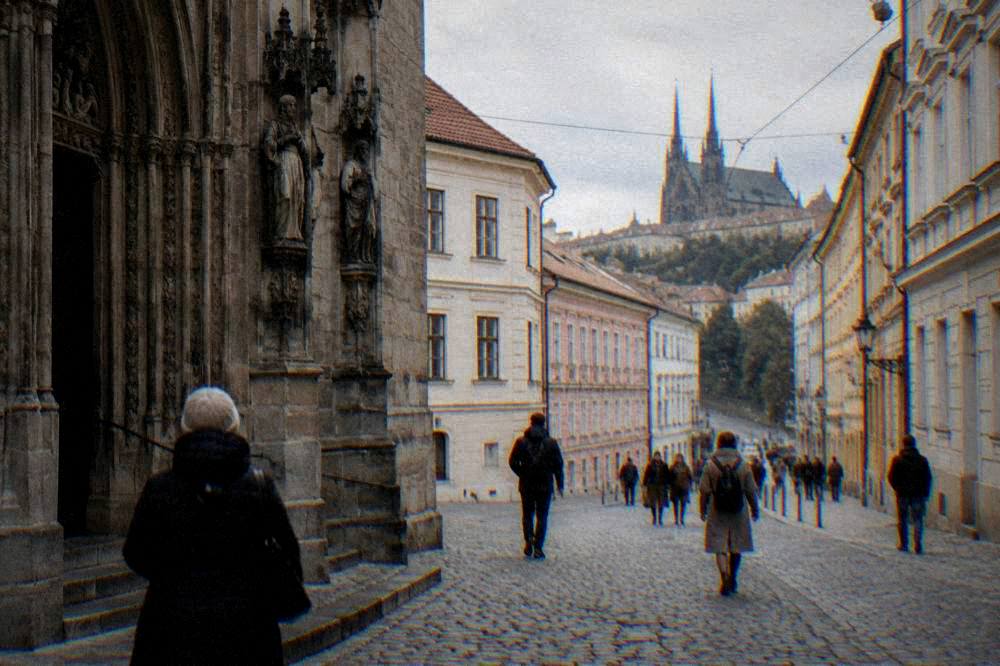 Stone church portal with carved detail and people passing on a cobbled street in Brno