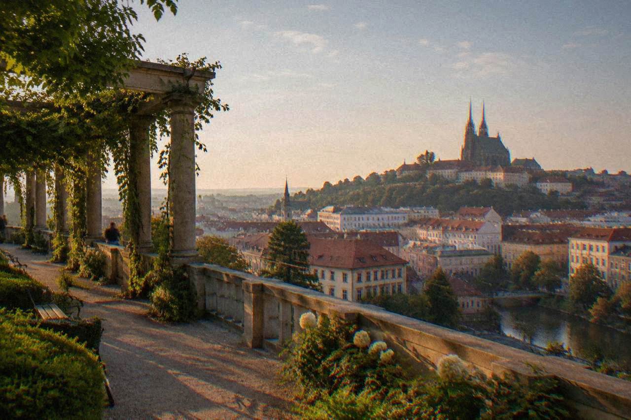 Terraced gardens with a stone colonnade overlooking the rooftops of Brno below a cathedral hill