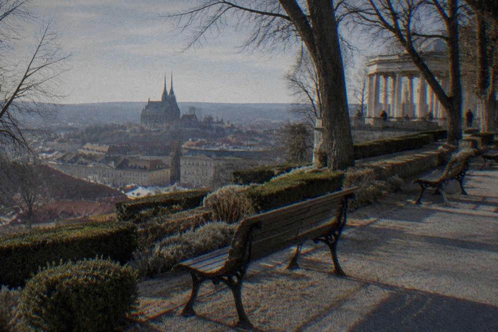 Park benches along a stone path beside planted terraces on a city hillside