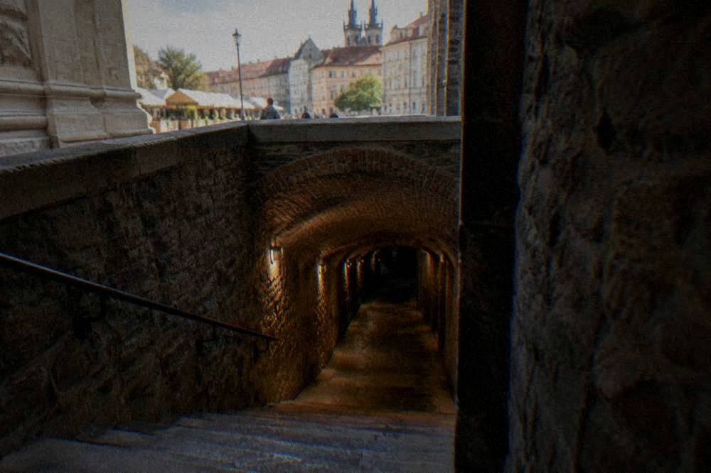 Stone staircase descending from a market square into a dim brick-vaulted cellar passage