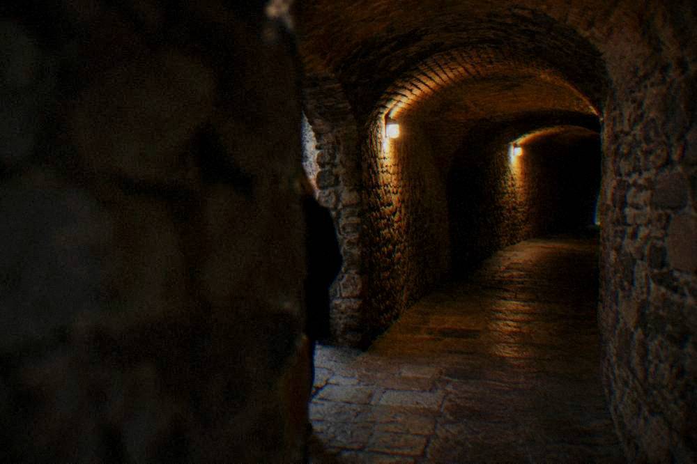 Narrow vaulted passage under stone houses lit by small warm lamps