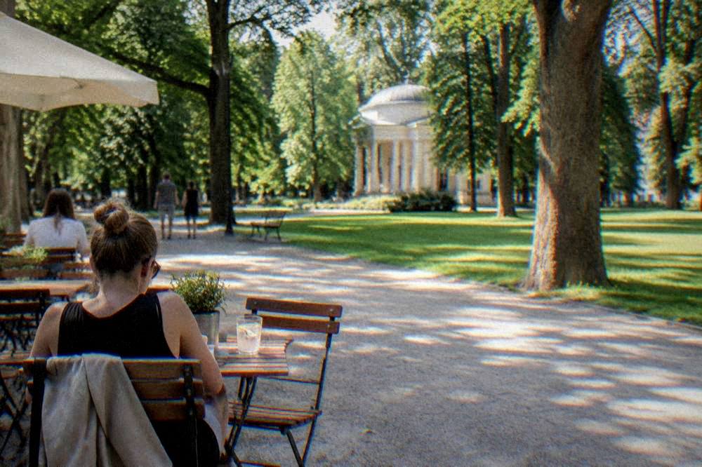 Outdoor cafe tables beside a park path with green trees behind