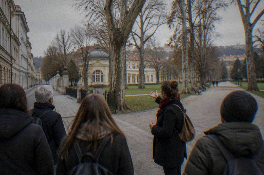 A guide speaking to a small group of visitors on a city street near a park entrance