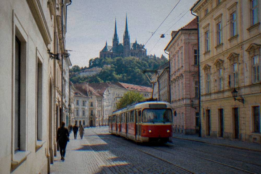 A red tram moving along a street with old buildings in Brno