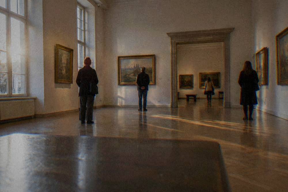 Visitors looking at framed paintings in a gallery hall