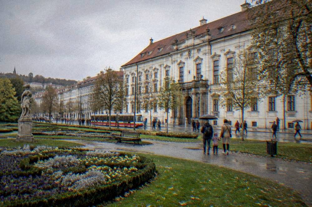 Families strolling a city park with flowerbeds and statues