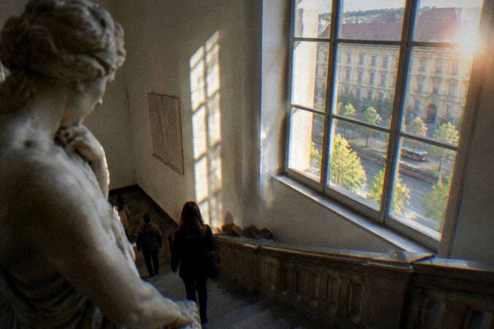 Gallery staircase lit by a tall window with sculpture in the foreground