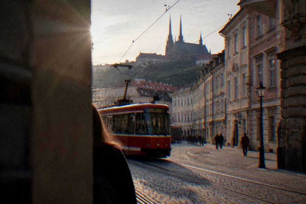 A red Brno tram passing historic buildings on a city street