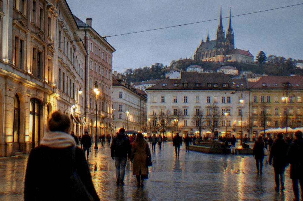 Visitors walking across a Brno square in the evening with illuminated facades