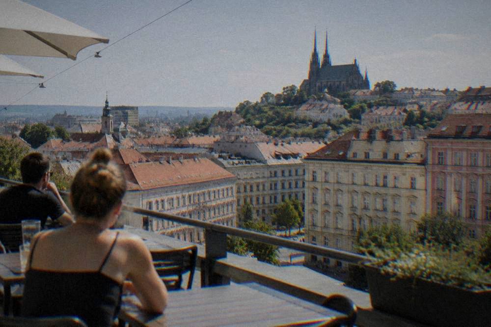Visitors on a terrace looking out over the rooftops and spires of Brno
