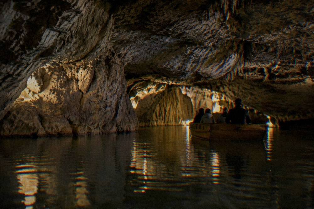 Wooden boat gliding on an underground river inside a lit cave passage
