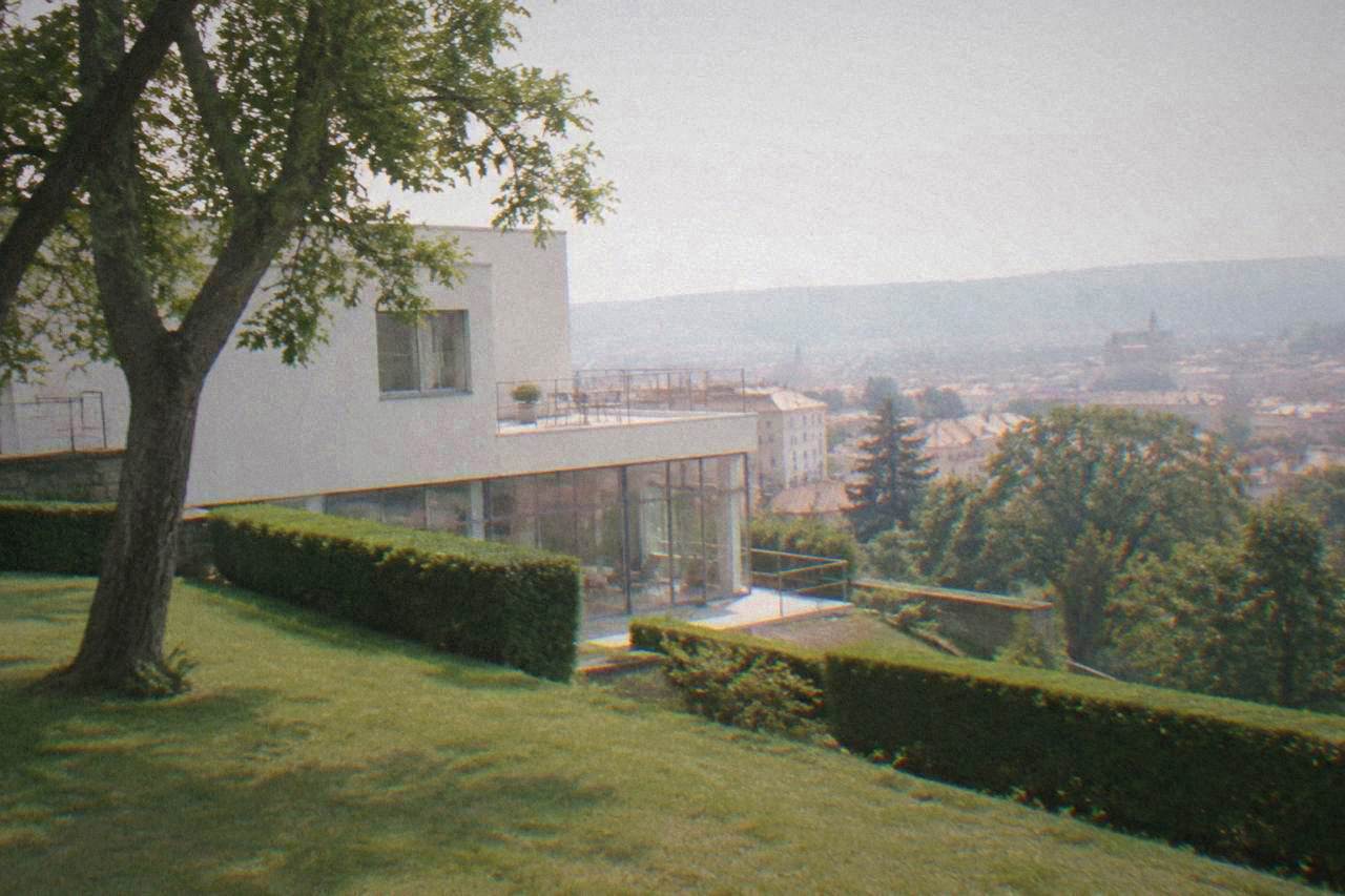 A pale functionalist villa with a flat roof and a garden of trimmed hedges in Brno
