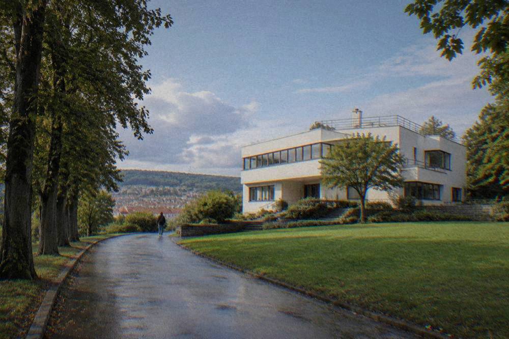 A villa driveway lined with trees leading to a light-coloured modernist facade