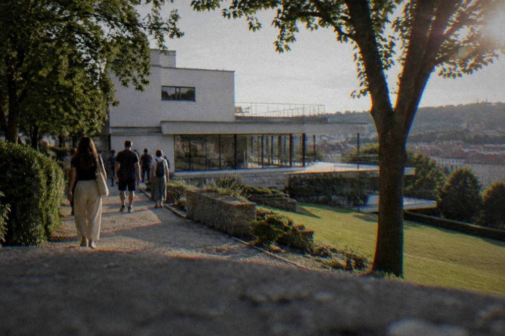 Tourists walking on a gravel path through the terraced garden of a white modernist villa