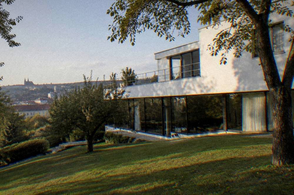 The garden facade of a white villa with large windows above a grassy slope