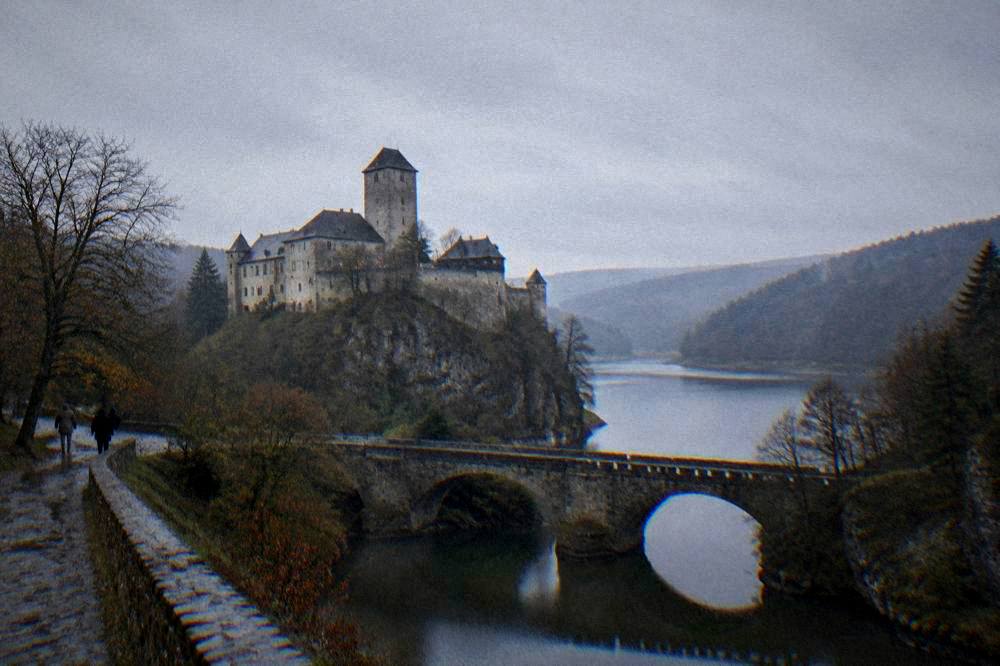An old stone bridge crossing a narrow river between valley walls at dusk
