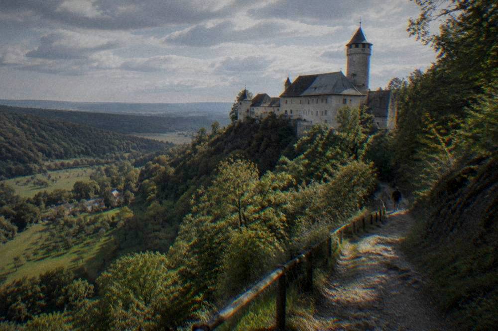 A forest path climbing a hill toward a distant castle tower