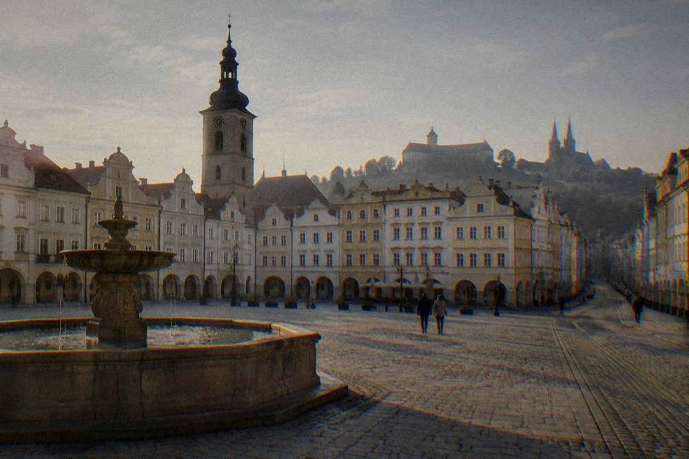 A castle on a hill above a city with twin-spired cathedral towers in the distance