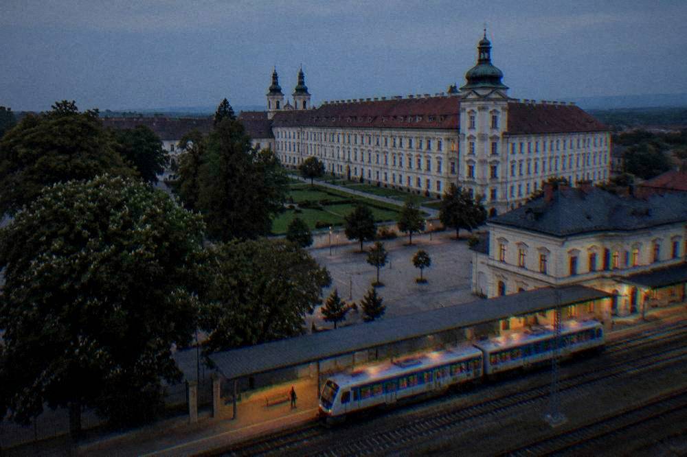 A Czech regional train waiting at a station platform beside a historic station building