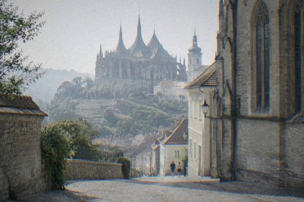 A large Gothic church with tall windows seen from a cobbled street in a Czech town