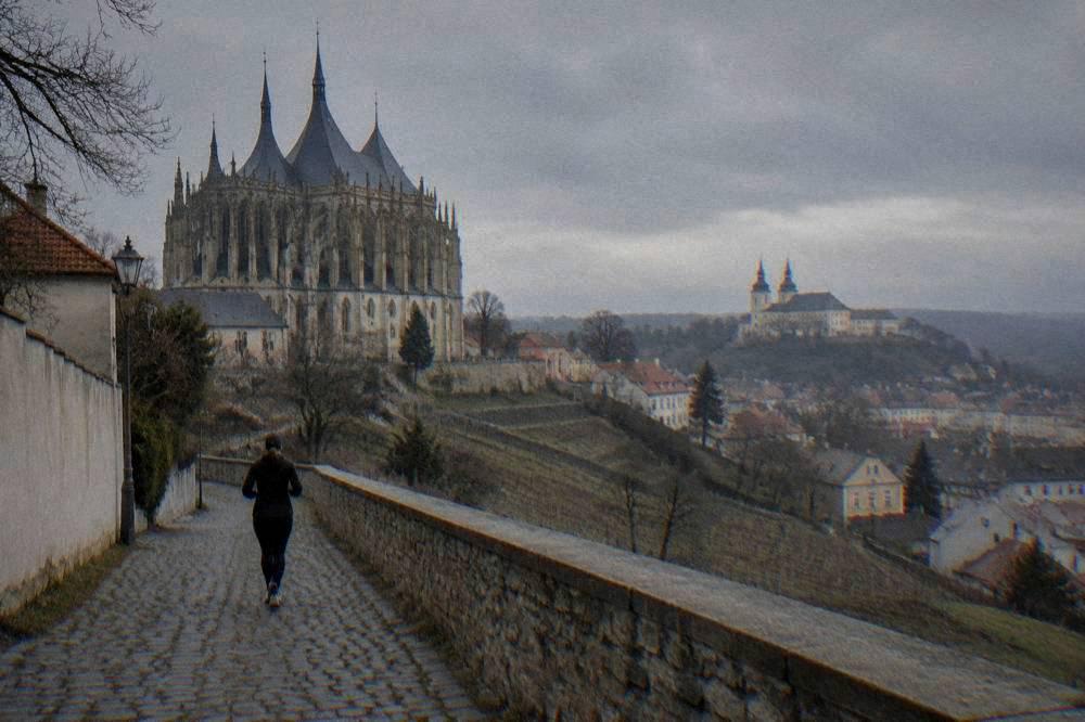 A castle on a hill above a city with twin-spired cathedral towers in the distance