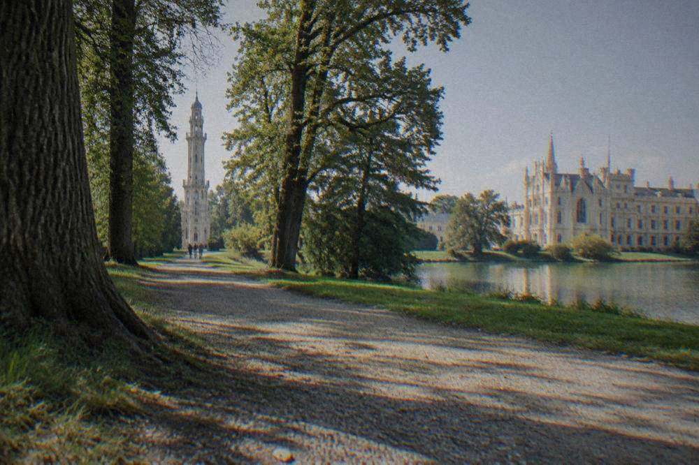 A gravel path leading through tall trees toward the minaret tower in the Lednice park